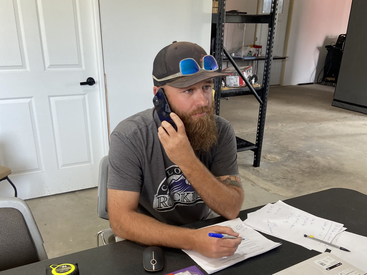 Mack on a phone call at the shop desk, taking notes